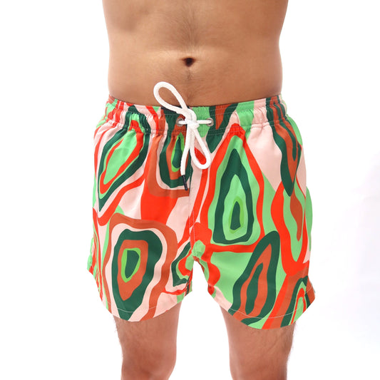 Colorful swim shorts with a abstract pattern worn by a person on a white background