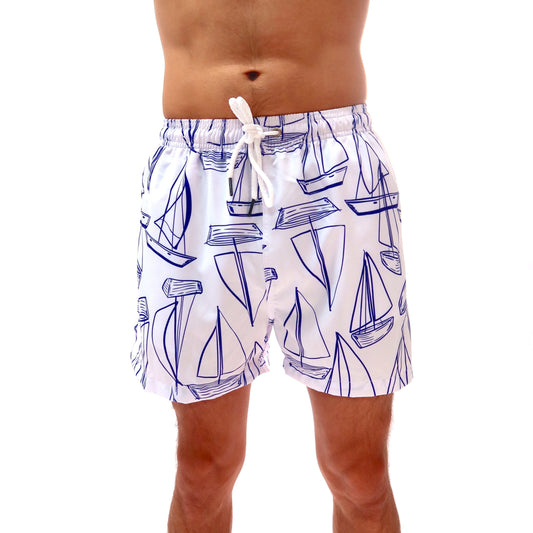 Person wearing white swim shorts with blue sailboat pattern on a plain background